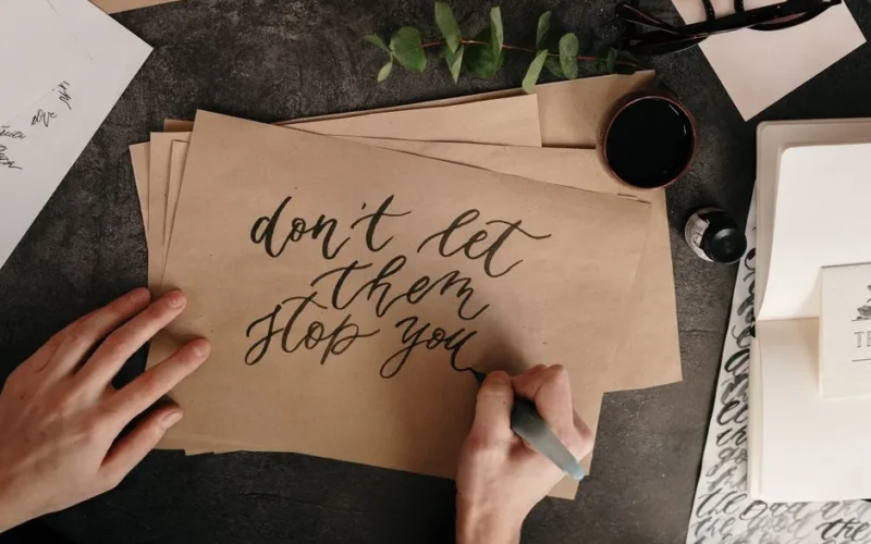 Hand writing motivational quote on textured paper with calligraphy tools.