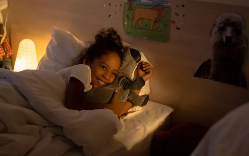 Young girl cuddles with her stuffed toy in a warmly lit bedroom, creating a serene bedtime atmosphere.