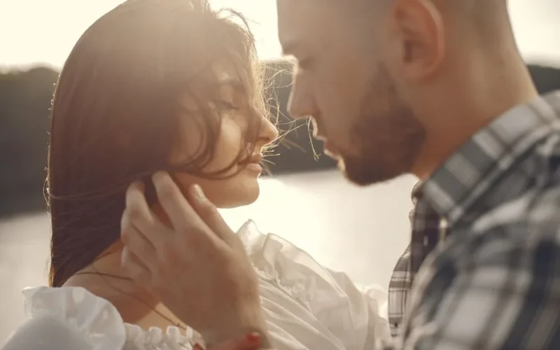 Close-up of a couple sharing an intimate moment outdoors at sunset.