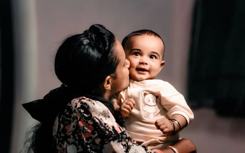 A heartwarming image of a mother kissing her smiling baby in a warm embrace.