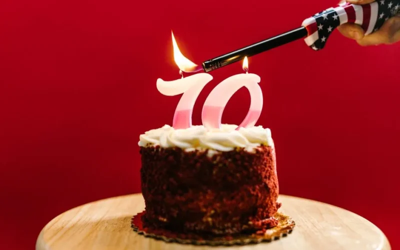 A close-up of a birthday cake with '70' candles being lit against a red background.