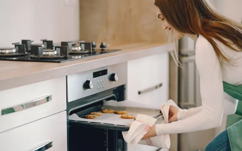 A woman pulls freshly baked cookies from an oven in a modern kitchen setting.