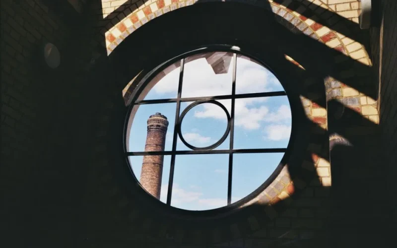 Circular window view highlighting a brick chimney against a clear blue sky.