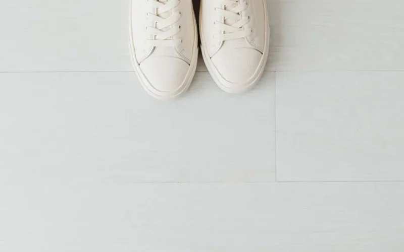 Close-up of white sneakers on a light wood floor with empty space.