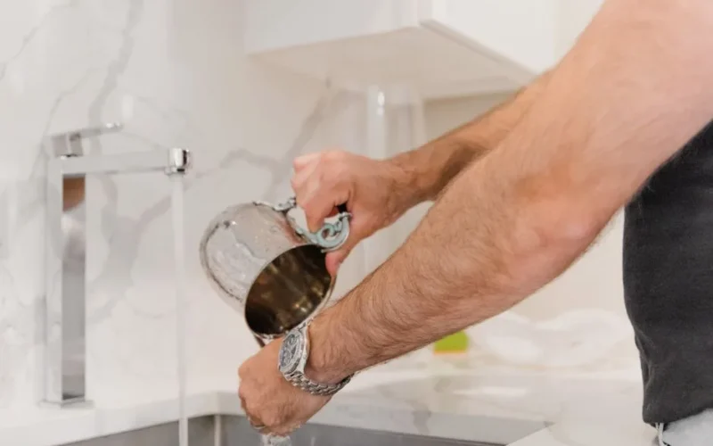 Close-up of a person washing a mug in a modern kitchen sink with running water.