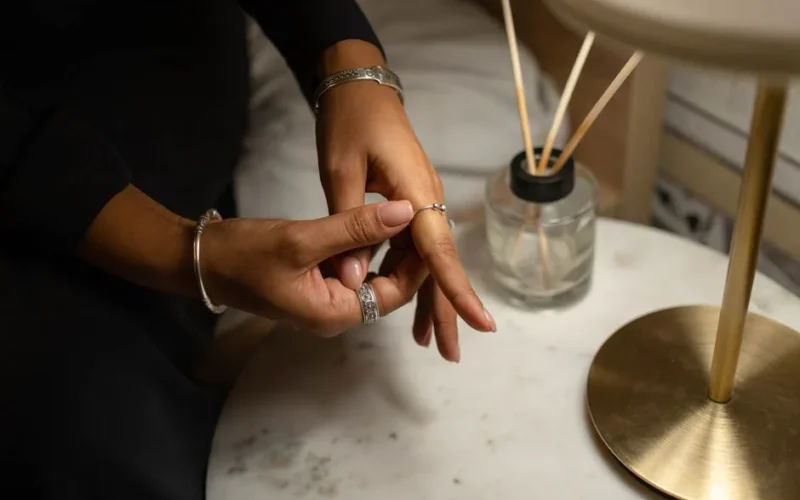Close-up of a hand with rings and bracelet, placed on a marble table, next to a diffuser.