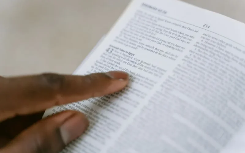 A person pointing to a passage in the Holy Bible, highlighting religious study.