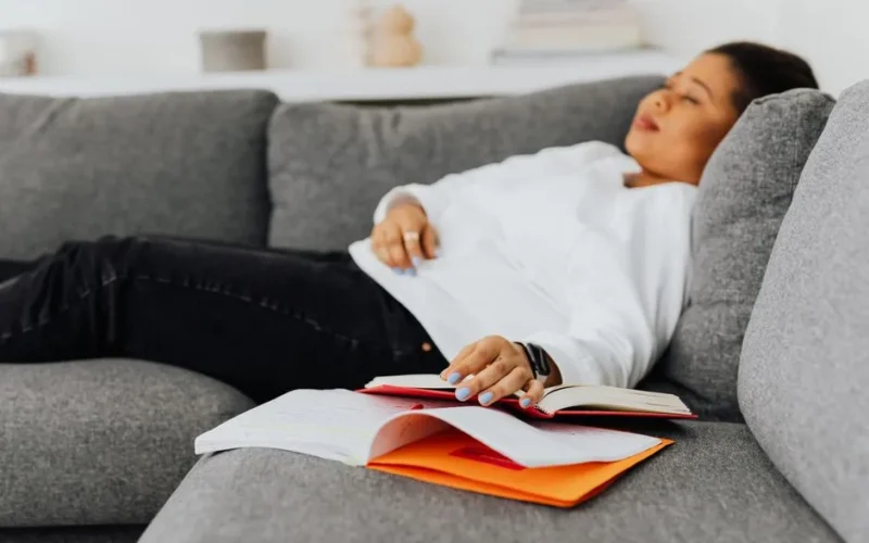 A student rests on a sofa with open books, embodying studying fatigue.