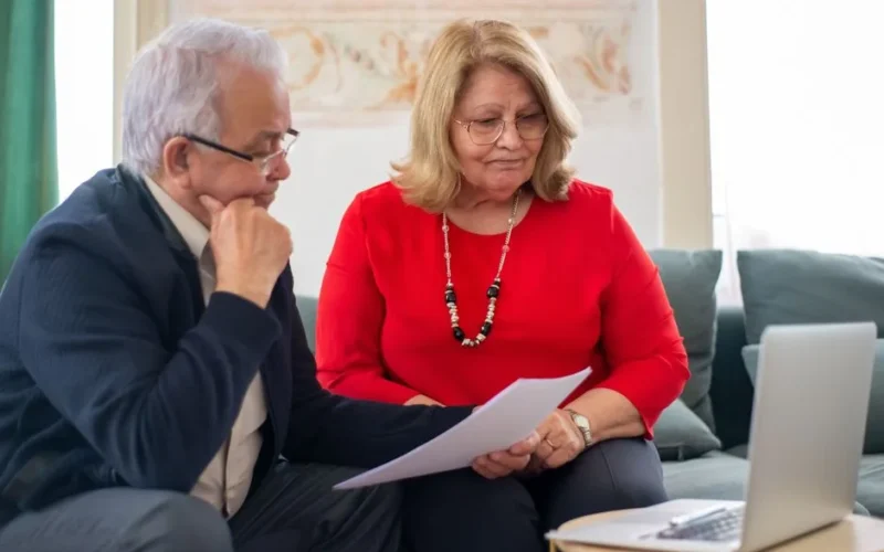 Elderly couple reviewing financial documents together at home in Portugal.