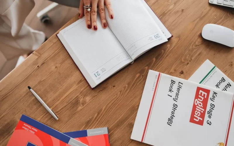 High angle view of a student studying with English literacy books and an open diary for note-taking.