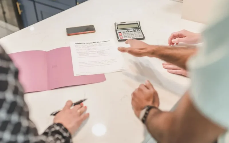 Hands gesturing during a real estate document review on a modern office desk with a calculator.
