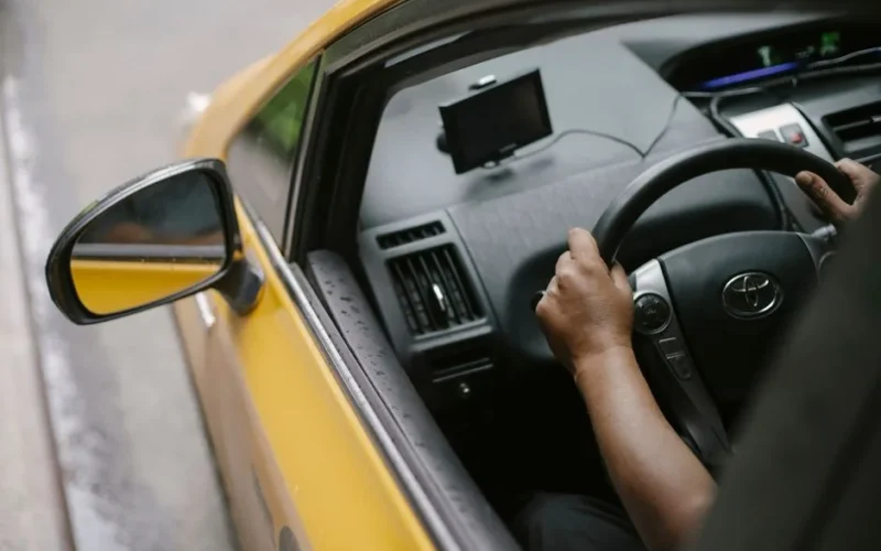 From above of crop unrecognizable person driving modern yellow taxi car with GPS navigator on city street in daytime