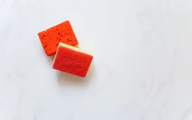 Two bright orange sponges suitable for cleaning against a white background.