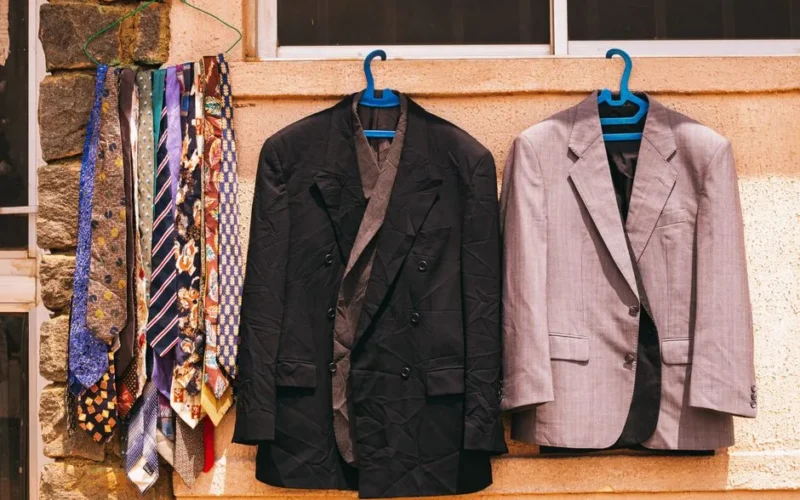 A black and gray suit with colorful ties hanging outdoors on a wall in Jos, Nigeria.