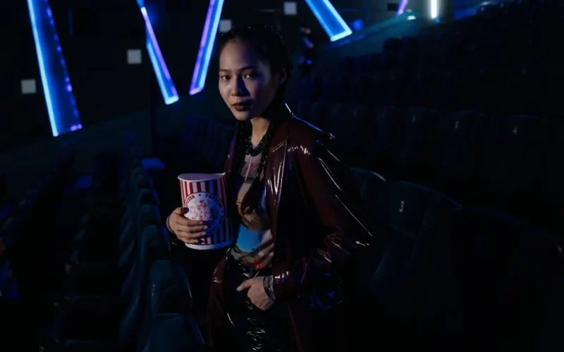 A stylish young woman holding popcorn in a dimly lit cinema, ready for a movie night experience.