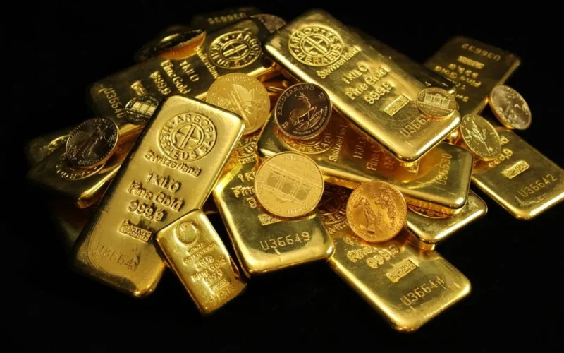 A close-up of gold bars and coins symbolizing wealth and investment on a black background.