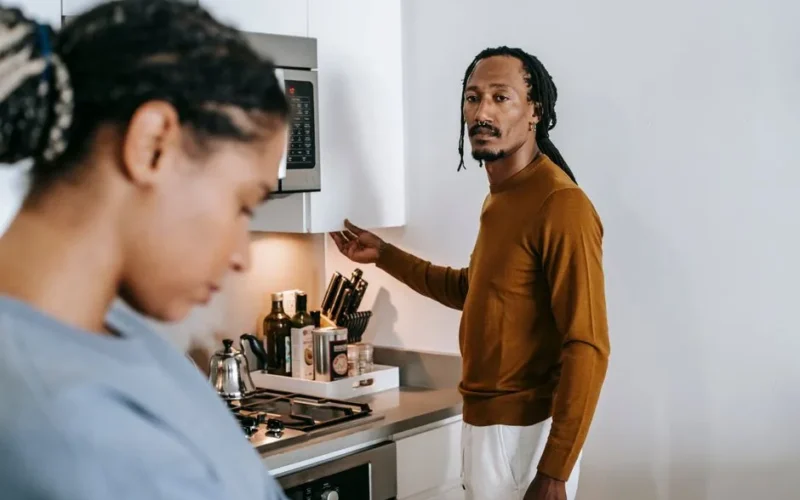 Young black couple in casual outfit standing at kitchen and arguing with each other at home