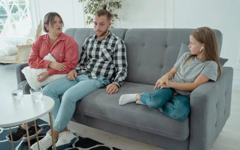 A family sits together on a sofa, discussing in a comfortable home setting, indicating a counseling session.