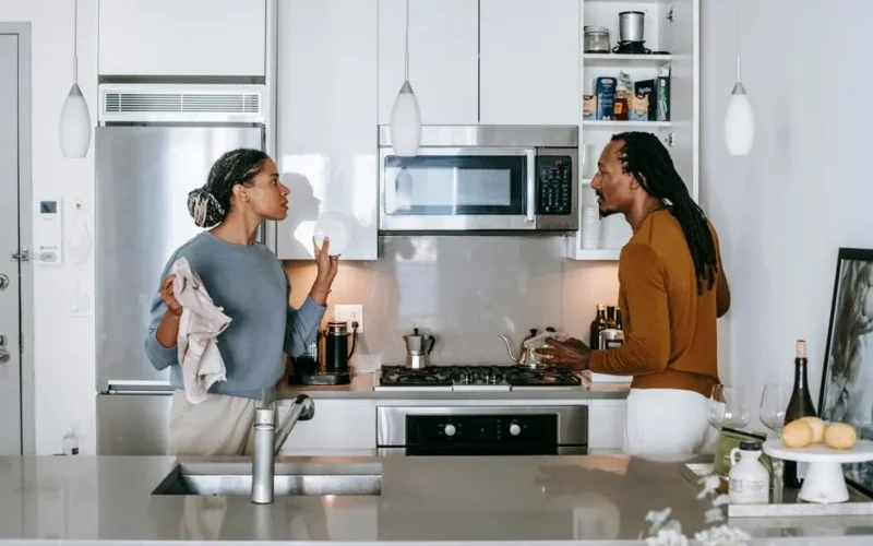 Young black woman talking to annoyed male partner while looking at each other during quarrel in house