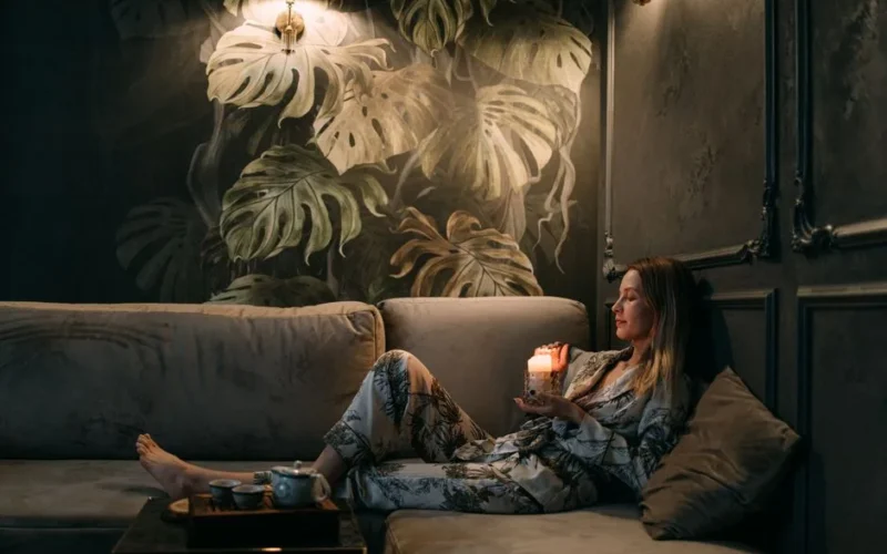 A woman relaxes on a sofa with a candle, creating a calming atmosphere indoors.