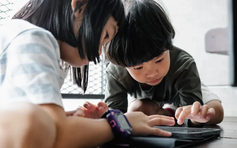 Two children focused on using a tablet indoors, engaging with technology for learning and play.