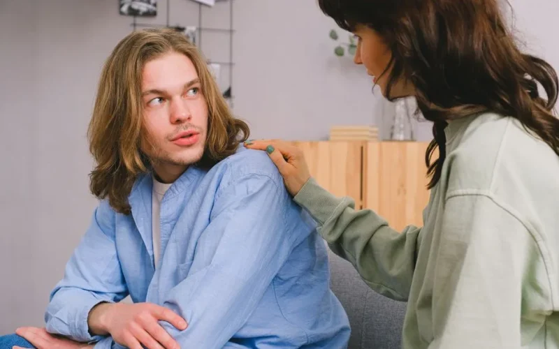 Concentrated woman talking and touching shoulder of pensive male in light room in daytime