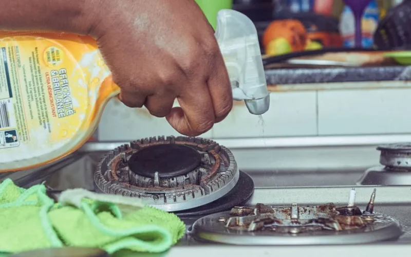 A detailed view of a hand cleaning a stovetop using a spray bottle and cloth.