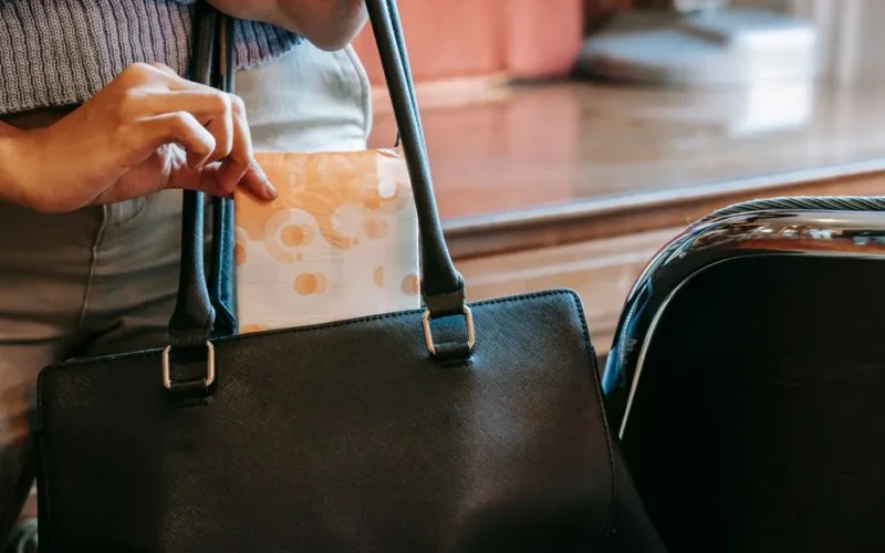 Crop anonymous female in casual wear putting sanitary pad in black leather handbag