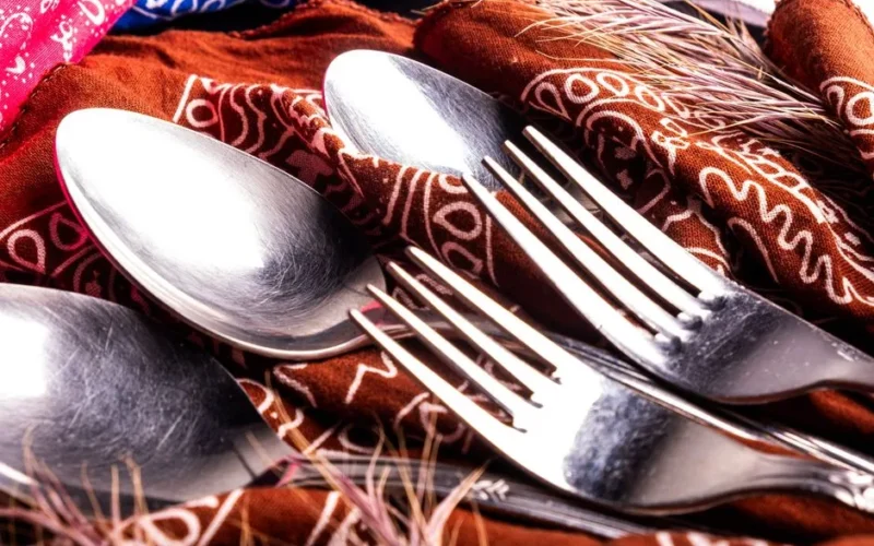Close-up of shiny silverware on patterned fabric with colorful cloth.