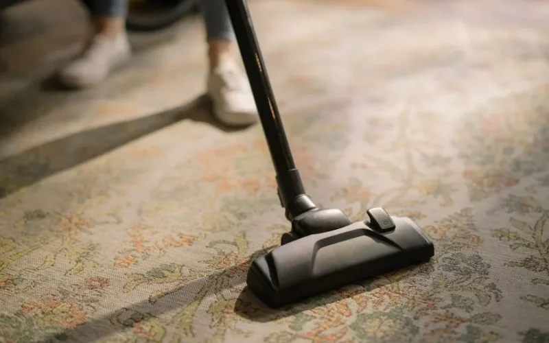 Close-up of a vacuum cleaner on a patterned carpet in a sunlit room, capturing a moment of household cleaning.