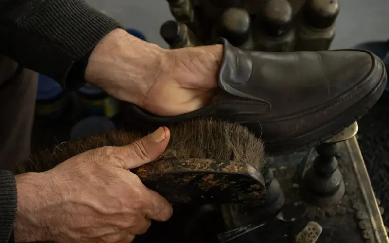 Detailed view of a shoe being polished by hand using a brush in a workshop setting.