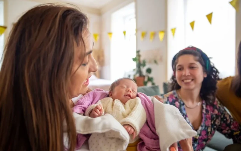Mother lovingly cradles her newborn baby, celebrating with family indoors.