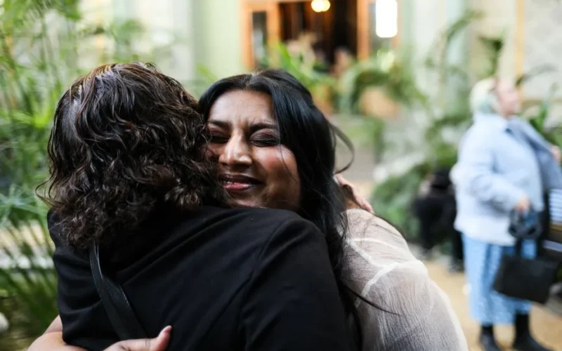 Two women embrace warmly in an indoor setting, surrounded by a vibrant atmosphere.
