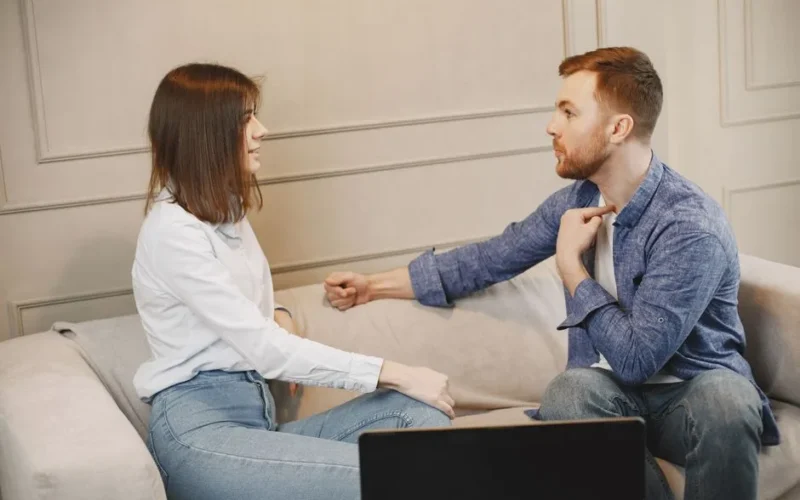 A young couple engaged in a conversation while sitting on a beige couch indoors.