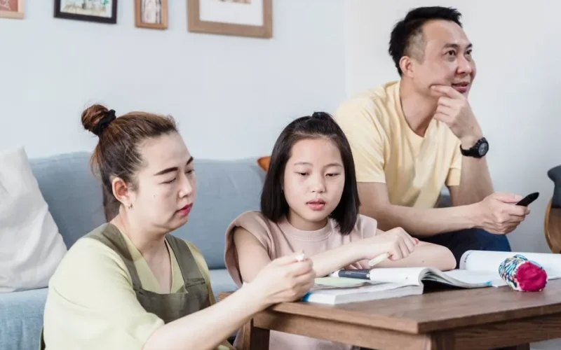 A family helping their daughter with homework in the living room, promoting togetherness.