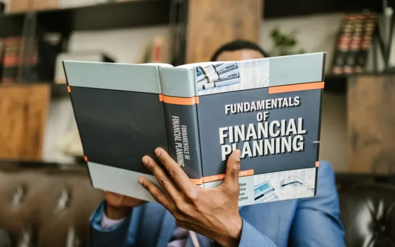 A professional individual in a suit reading 'Fundamentals of Financial Planning' indoors.