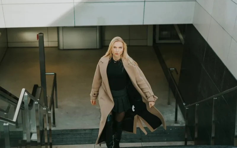 Fashionable woman in Berlin wearing a wool coat and boots, elegantly walking down steps.