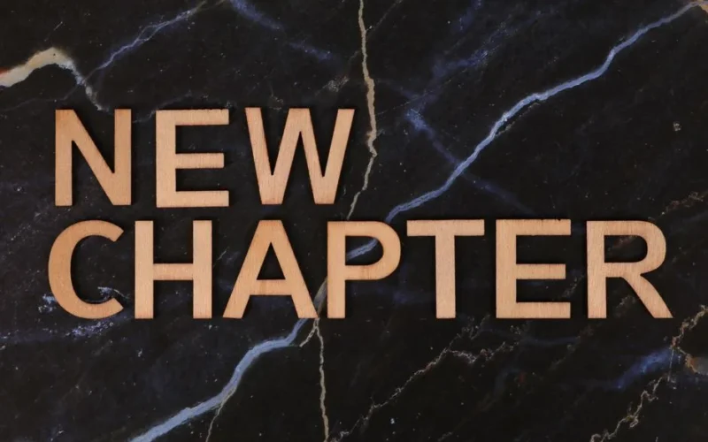 Wooden letters spelling 'New Chapter' on a dark marble background symbolize fresh beginnings.