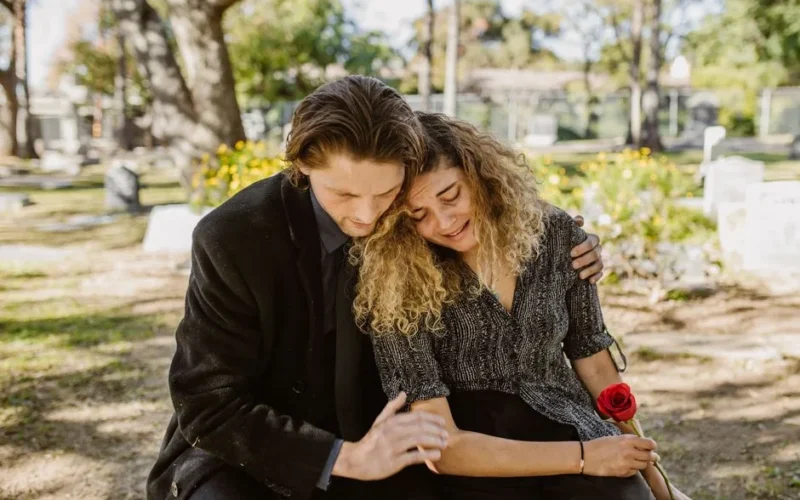 A comforting embrace in a serene graveyard captures grief and support.