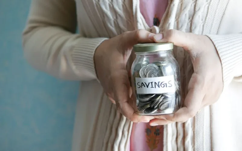 Woman holding a jar labeled 'savings' filled with coins, representing financial savings.