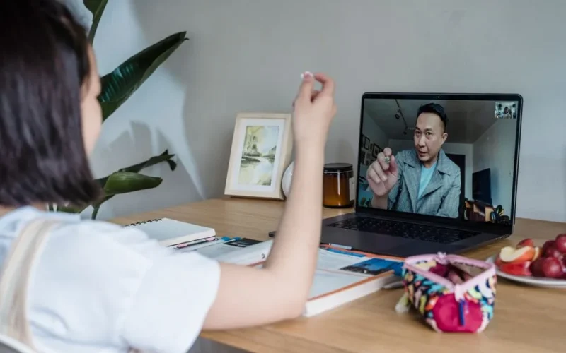 Child attends an online class with a teacher via video call on a laptop.