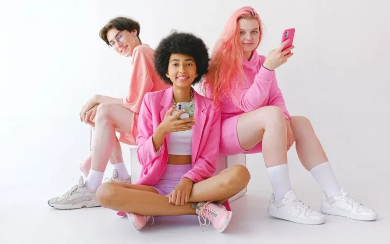 Full body of multiethnic happy teenage girls with mobile phones and boy looking at camera and smiling on white background