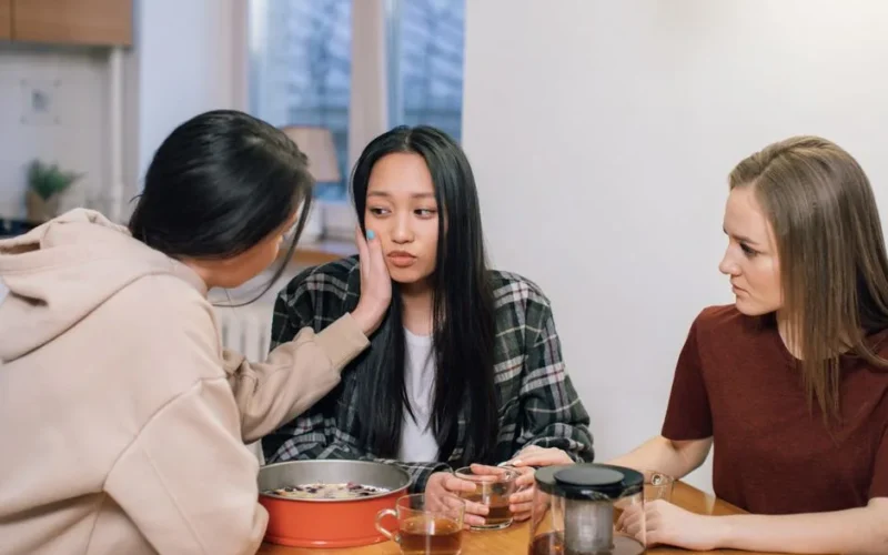 Three women at a table offering emotional support and comfort to a friend, fostering compassion and empathy.