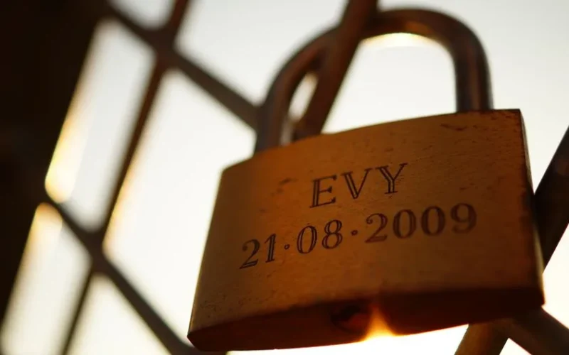 Golden padlock engraved with 'EVY 21.08.2009' on a fence, symbolizing love.