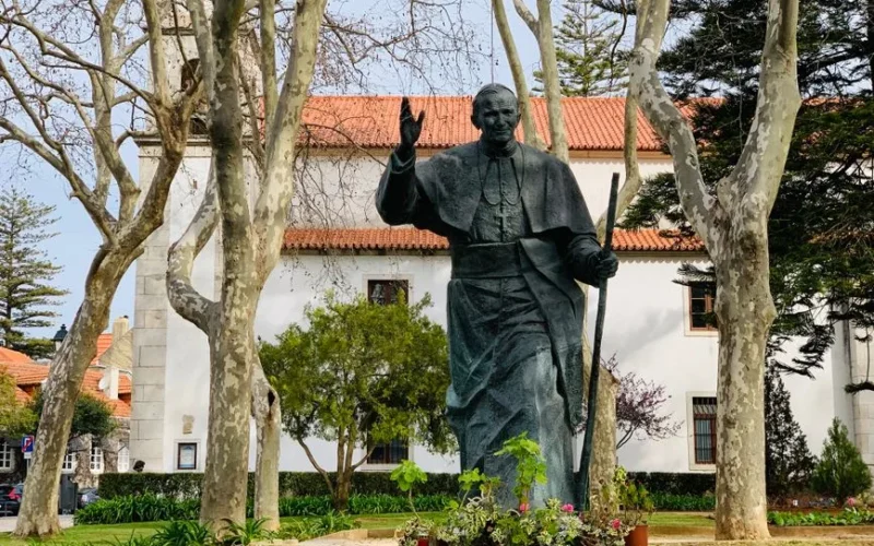 A statue of John Paul II surrounded by trees in a tranquil urban park setting.