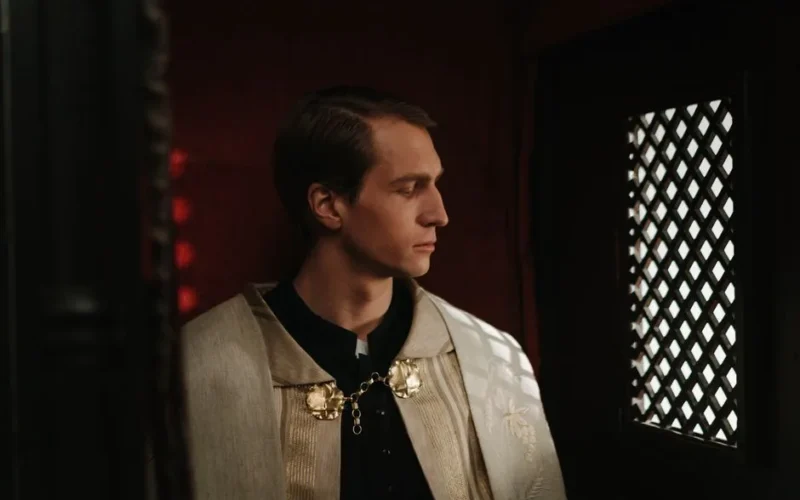 A priest in a traditional vestment sits in a confessional box, reflecting quietly.