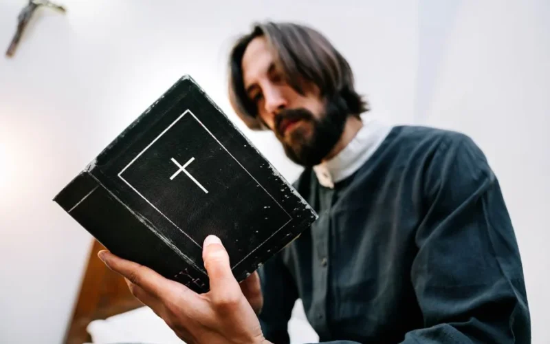 A priest reading a Bible, symbolizing faith and devotion in a serene indoor setting.
