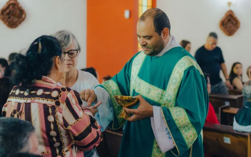A priest in a green vestment distributing Holy Communion to parishioners during a church service.