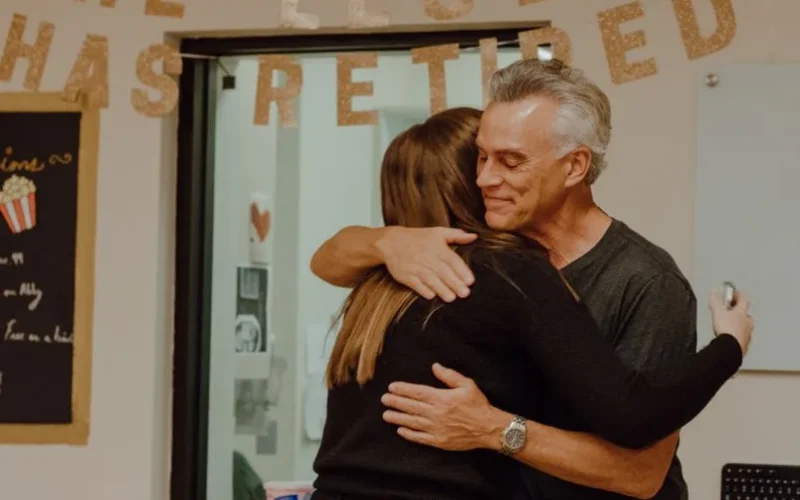 A heartfelt moment as two people embrace at a retirement party with festive decor.