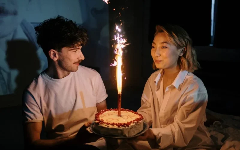 Couple celebrating a birthday with a cake and sparkling candle indoors, captured in a warm, intimate setting.